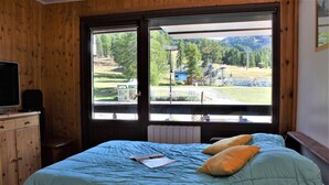 Une chambre à coucher avec un lit, une commode en bois et une fenêtre donnant sur un paysage verdoyant et un bâtiment.