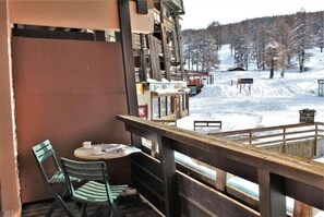A balcony with a table and chairs, overlooking a snowy landscape with a ski slope and buildings in the background. - 10m from resort center, 1st floor, balcony, tv, ski locker, 23m², Risoul (Risoul)