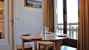 A dining area with a round table, four chairs, and a window with curtains. - 20m from ski slopes, 3rd floor, balcony, tv, ski locker, 21m², Risoul (Risoul)