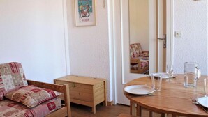 A cozy room with a wooden sofa, a small wooden chest, a dining table with plates and glasses, and a framed poster on the wall. - 20m from ski slopes, 3rd floor, balcony, tv, ski locker, 21m², Risoul (Risoul)