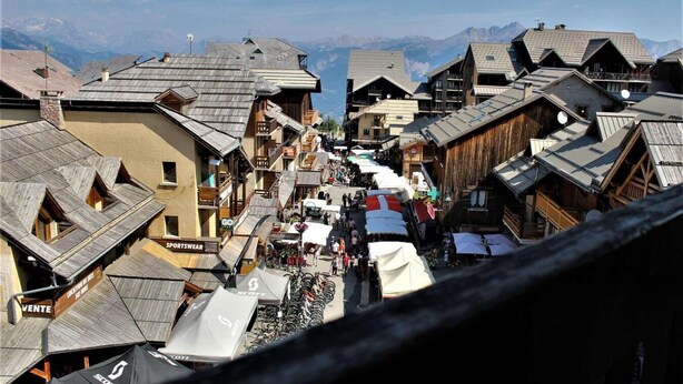 A narrow street lined with wooden buildings, some with balconies, and a mountain backdrop. - 20m from ski slopes, 3rd floor, balcony, tv, ski locker, 21m², Risoul (Risoul)