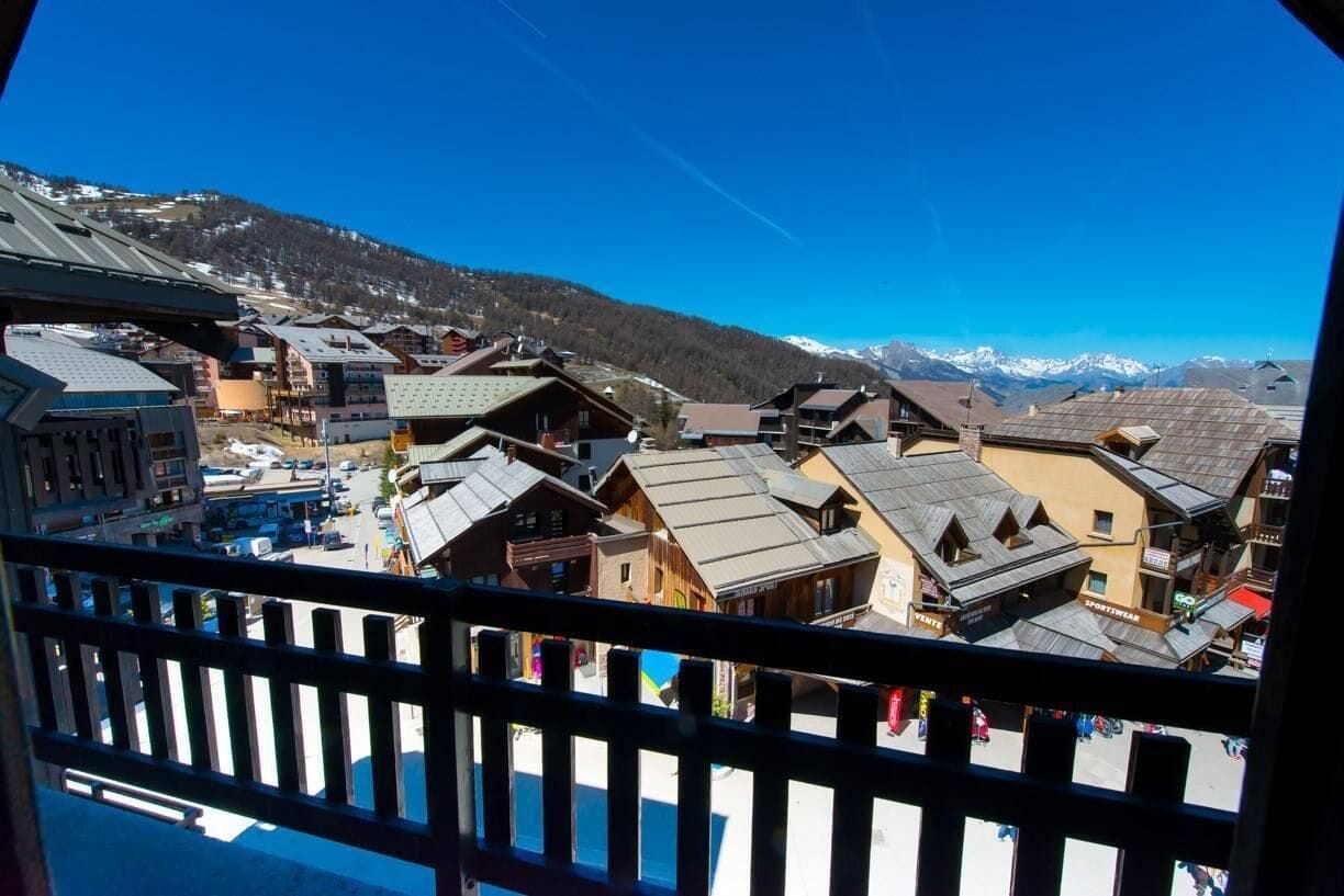 Eine Bergstadt mit traditionellen Holzbauten, wolkenlosem Himmel und schneebedeckten Bergen im Hintergrund.