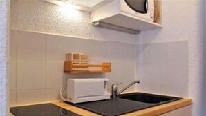 A compact kitchen with a built-in microwave, a sink, and a portable induction cooktop. - 20m from ski slopes, 3rd floor, balcony, tv, ski locker, 21m², Risoul (Risoul)