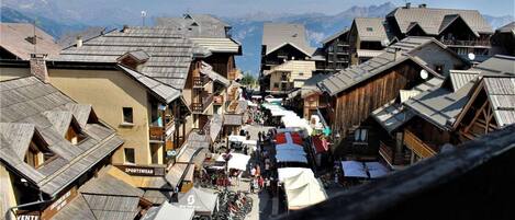 A narrow street lined with wooden buildings, some with balconies, and a mountain backdrop.