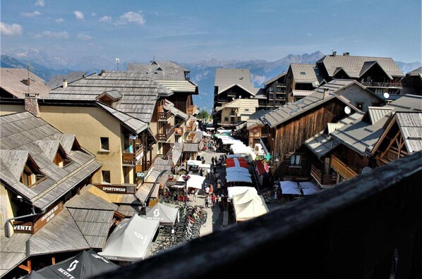 A narrow street lined with wooden buildings, some with balconies, and a mountain backdrop.