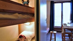 Une chambre avec un lit superposé, un jouet en peluche, une petite table et une fenêtre avec des rideaux.