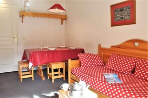 A room with a bed, a table with a red tablecloth, a small wooden stool, a wall-mounted shelf with a lamp, and a framed picture on the wall. - 300m from resort center, 2nd floor, balcony, ski locker, 26m², Risoul (Risoul)