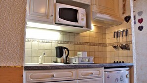 Eine Küche mit weißen Schränken, einer Mikrowelle, einer Kaffeemaschine und einem Kühlschrank.