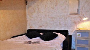 Ein Einzelbett mit schwarz-weißer Bettwäsche, ein kleiner Nachttisch mit Lampe sowie eine wandmontierte Klimaanlage.
