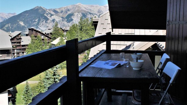 Eine Holzterrasse mit Tisch und Stühlen, mit Blick auf eine gebirgige Landschaft und Gebäude im Hintergrund.