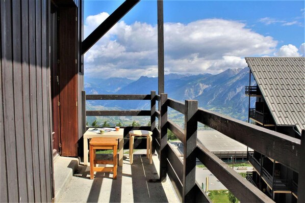 Relax on the balcony with a serene mountain view, featuring a table and chairs for dining or unwinding.