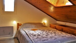 Un dormitorio con techo inclinado, una cama con manta estampada, lámparas de noche, un aparador de madera y una ventana.