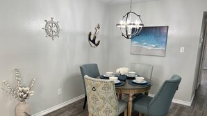 A dining area with a round table, four chairs, a chandelier, a wall-mounted painting, and decorative wall art. - Lovely 1 Bedroom walking distance from Beach! (Galveston)