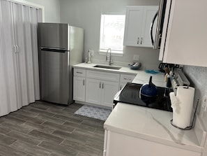 Une cuisine moderne avec un réfrigérateur en acier inoxydable, des armoires blanches, une cuisinière noire et une fenêtre équipée de stores.