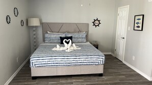 A bedroom with a bed, a nightstand, a wall clock, and a door. - Lovely 1 Bedroom walking distance from Beach! (Galveston)