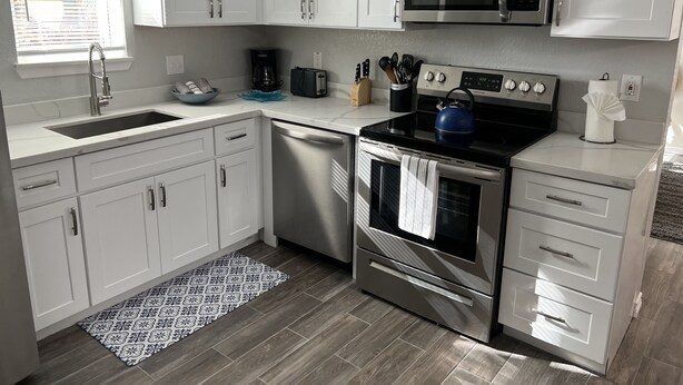 A modern kitchen with white cabinets, stainless steel appliances, and a patterned rug. - Lovely 1 Bedroom walking distance from Beach! (Galveston)
