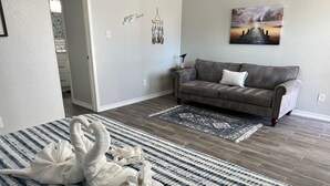 A bedroom with a bed, a gray sofa, a patterned rug, and a wall with a painting. - Lovely 1 Bedroom walking distance from Beach! (Galveston)