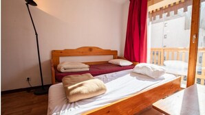 A bedroom with a wooden bed, two pillows, a red curtain, and a view of a wooden deck through a glass door.