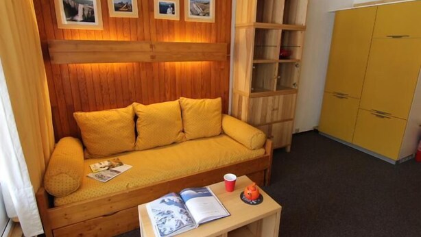 Une pièce avec un mur recouvert de panneaux de bois, un canapé jaune, une armoire en bois et une commode jaune.