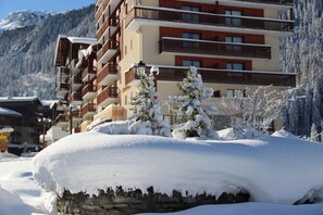 A multi-story hotel with balconies, snow-covered trees, and a mountainous backdrop.