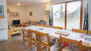 A dining area with a large table, wooden chairs, and a sofa. There is a television on a stand and a window with a mountain view. - 70m from ski slopes, 1st floor, view mountain, parking, tv, ski locker, 46m², Valfréjus (Valfréjus)
