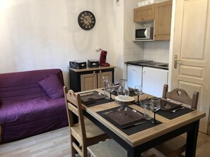 Un comedor con una mesa de madera dispuesta para cuatro, un sofá morado, un microondas y un reloj en la pared.
