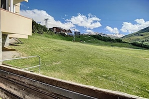 Un espace extérieur verdoyant avec un banc en bois, un bâtiment doté d’un balcon et une vue sur les montagnes en arrière-plan.
