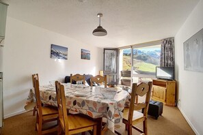 Un'area pranzo con un tavolo rotondo apparecchiato per quattro persone, sedie in legno, una lampada a soffitto e una finestra con vista su un paesaggio montuoso.
