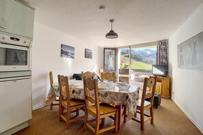 Een eetgedeelte met een tafel voor vier personen, houten stoelen, een oude oven en een televisie op een houten kast.