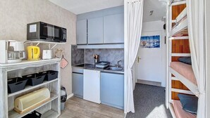 A compact kitchen with a microwave, kettle, and sink. There is a small refrigerator and a shelf with storage bins. A bunk bed with a curtain is visible in the background. - Ski-in/ski-out & foot of the slopes, 13rd floor, balcony, tv, ski locker, 20m², Les Menuires (Les Menuires)