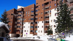Un hôtel à plusieurs étages doté de balcons, avec une piste de ski en arrière-plan et un ciel bleu dégagé.