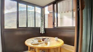 Une pièce d’angle avec une table et des chaises en bois, une fenêtre donnant sur une montagne et un rideau.