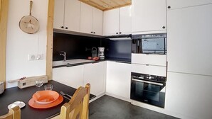 Una cocina compacta con armarios blancos, una encimera negra y un techo de madera.