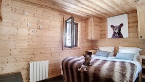 Un dormitorio de cabaña de madera con una cama, una ventana, un cuadro de un oso y un radiador.