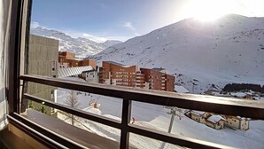 Vista desde una ventana sobre un paisaje montañoso nevado con edificios y cielo despejado.