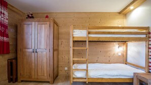 Een slaapkamer met een houten stapelbed, een garderobe en een kleine tafel.