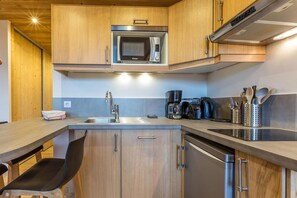 A compact kitchen with wooden cabinets, a built-in microwave, a coffee maker, and a dishwasher.