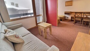 Um quarto aconchegante com sofá, uma mesa pequena, um espaço de refeições com bancos e vista para um edifício pela janela.