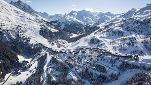 Uma aldeia montanhosa coberta de neve, com estradas sinuosas e construções aninhadas entre as árvores.