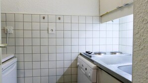 Uma cozinha compacta com paredes revestidas de azulejos brancos, máquina de lavar louça embutida e uma pia com bancada de metal.