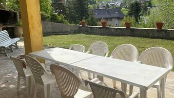 A covered patio with a table and chairs, overlooking a mountainous landscape.