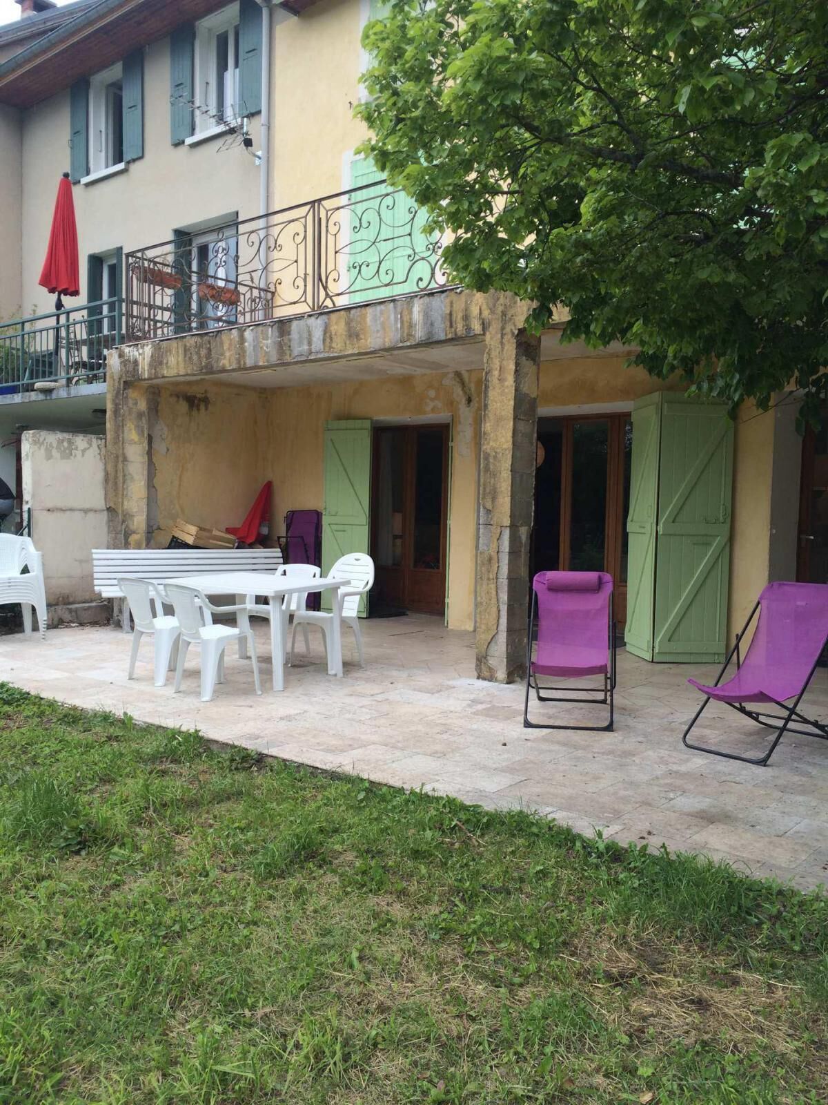 Zona de pati amb taula i cadires, una cadira morada i un para-sol vermell.