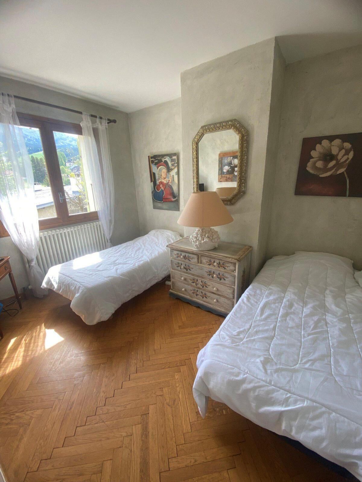 A room with two beds, a dresser, a window with curtains, and a radiator.