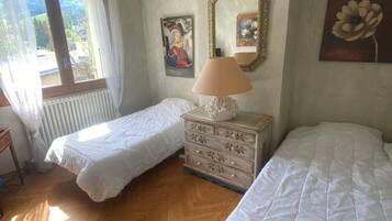 A room with two beds, a dresser, a window with curtains, and a radiator.