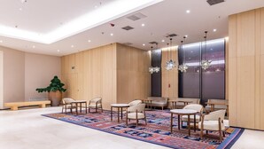 Un hall d’entrée spacieux, doté d’un tapis à motifs, de plusieurs espaces aménagés pour s’asseoir et d’un éclairage suspendu.