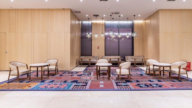 Une salle de conférence dotée d’un tapis à motifs, de murs recouverts de panneaux en bois et d’un éclairage moderne suspendu au plafond.
