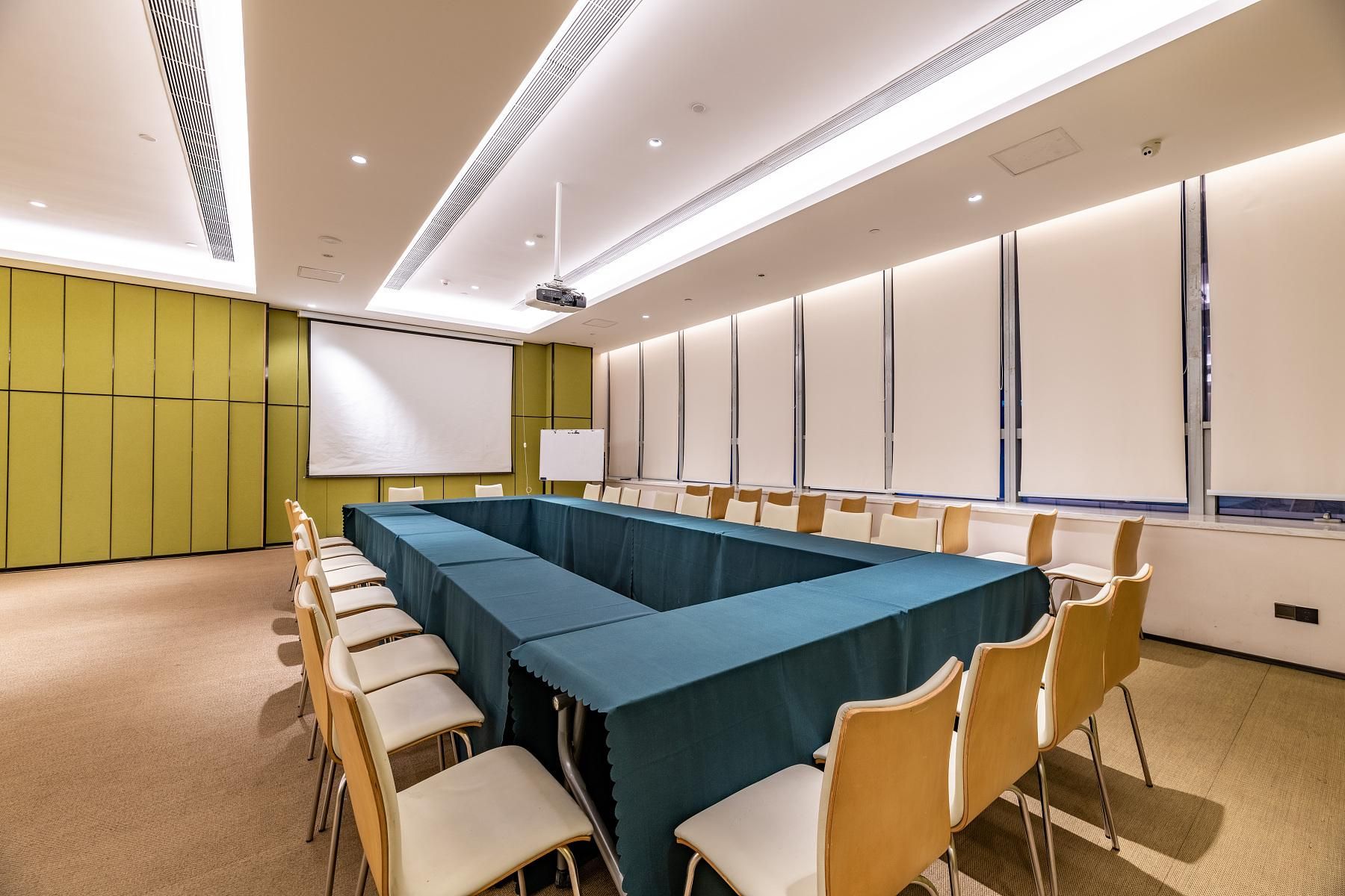 Un salón de conferencias con una larga mesa, sillas, una pantalla de proyector y una pizarra.