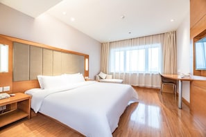 A hotel room with a large bed, a desk, a chair, and a window with curtains.