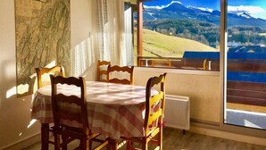 A dining area with a table and chairs, a map on the wall, and a large window with a mountain view. - 3rd floor, view mountain, balcony, tv, 33m², Villard de Lans (Villard-de-Lans)