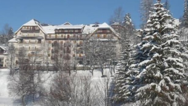 Ein großes, mehrstöckiges Gebäude mit einer symmetrischen Fassade, umgeben von schneebedeckten Bäumen und einem klaren Himmel.